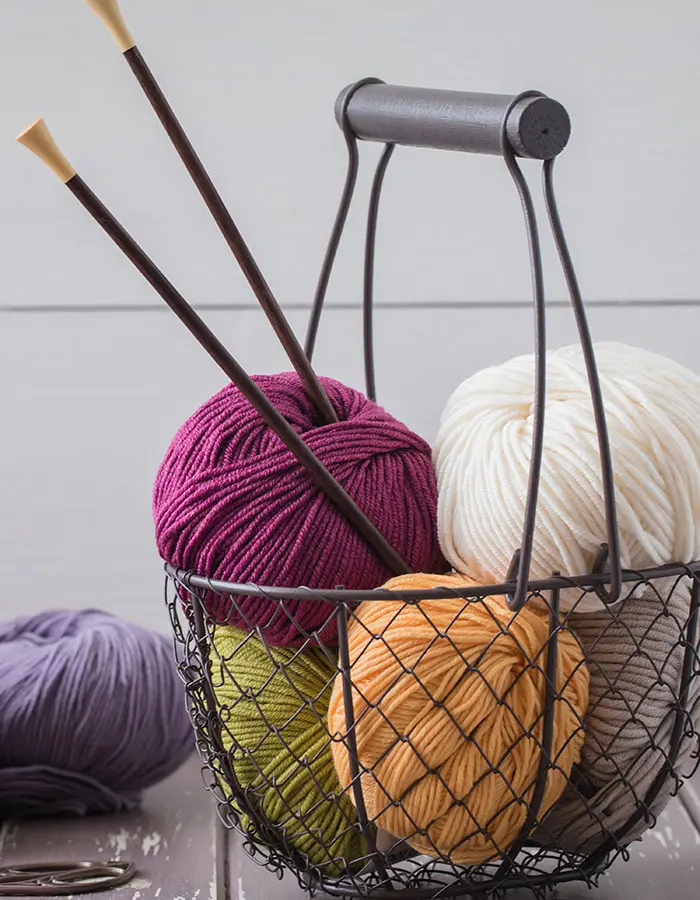 Colorful spring wool yarn in an iron basket with wooden knitting needles